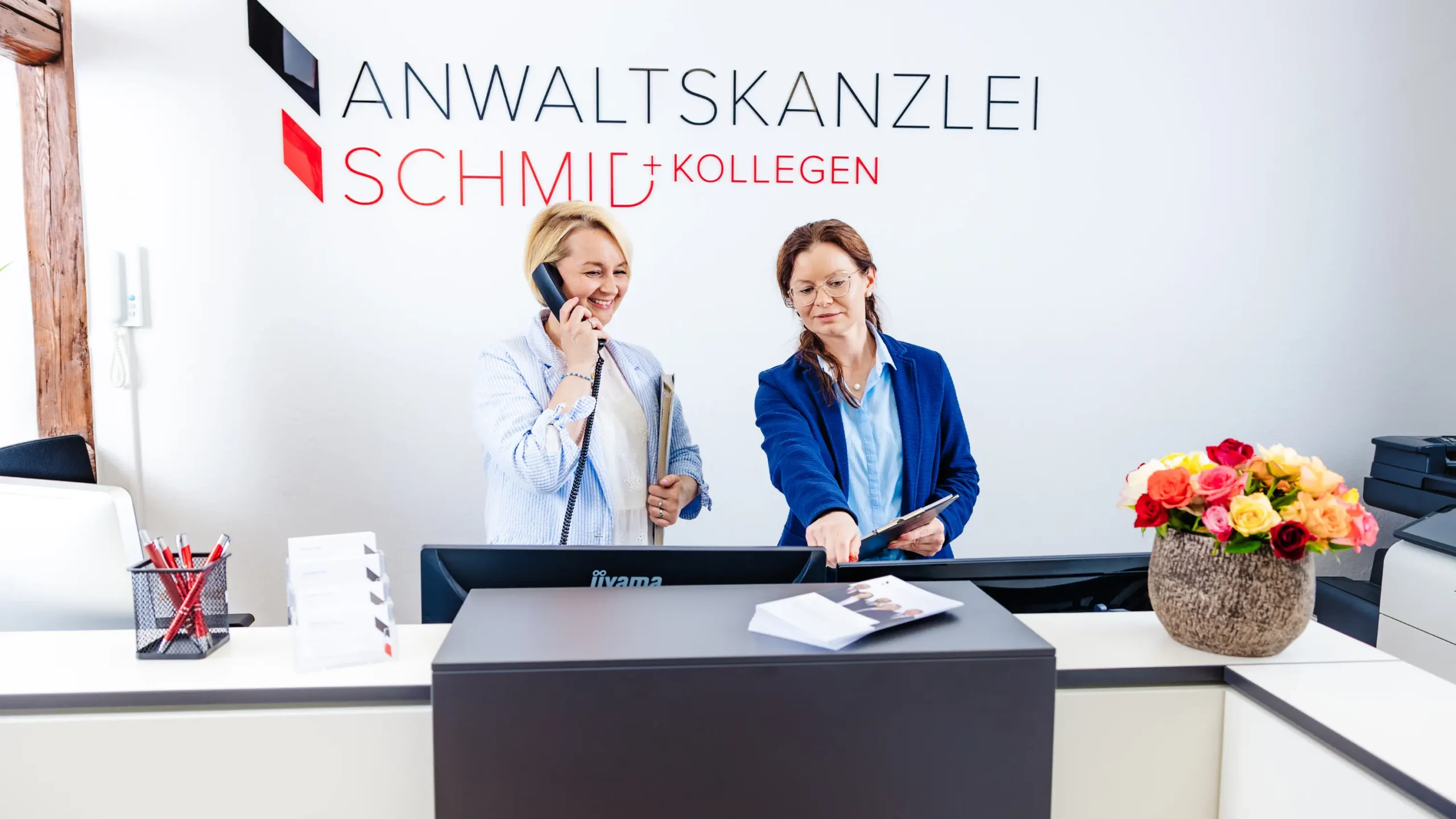 Kontakt zur Anwaltskanzlei Schmid und Kollegen aufnehmen Zwei Mitarbeiterinnen am Empfang der Anwaltskanzlei Schmid, eine telefoniert